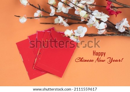 Happy Chinese New Year card with text, white flower branch and red envelopes on light orange background. Chinese New Year card backgrounds. Happy Chinese New Year.