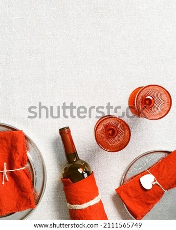 Festive table setting for Valentines Day romance dinner with two red colored wine glasses, trendy plates, bottle of wine, red linen napkins on table with tablecloth, copy space, top view, flat lay