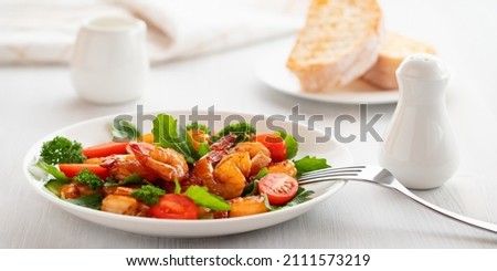 Fresh salad of shrimps, tomatoes, arugula and herbs on a white plate