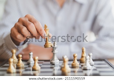 businessman hand moving gold Chess King figure and Checkmate opponent during chessboard competition. Strategy, Success, management, business planning, disruption and leadership concept Royalty-Free Stock Photo #2111590559