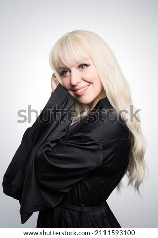 A beautiful young blond woman with a long wavy hair in a silky robe, with a glowing skin, isolated on a grey background