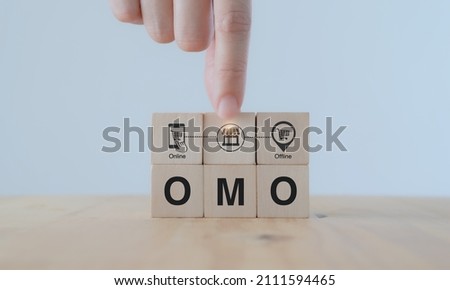 Online merge offline (OMO) concept. Borderless marketing channel conbination strategy creating new opportunities, sales increasing. Hand puts wooden cubes with combination of online and offline icon. Royalty-Free Stock Photo #2111594465