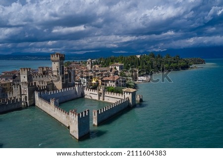 Aerial view on Sirmione sul Garda. Italy, Lombardy. Cumulus clouds over the island of Sirmione. Aerial photography with drone. Rocca Scaligera Castle in Sirmione.