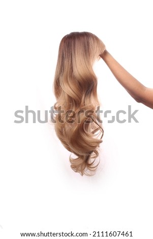 A hand holding a dirty blond synthetic wig, isolated on white background Royalty-Free Stock Photo #2111607461