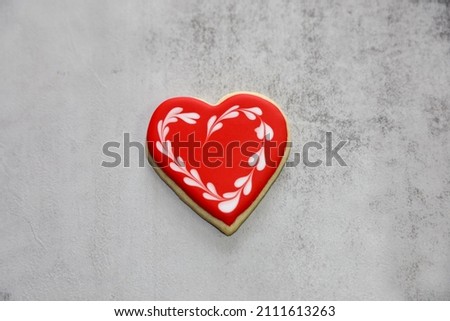 A heart-shaped sugar cookie with red royal icing and white heart wreath around it for valentine's day.