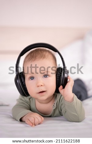 charming baby lying on a white background in headphones listens to music. infant 3 month old with headphones young DJ, baby's ear for music