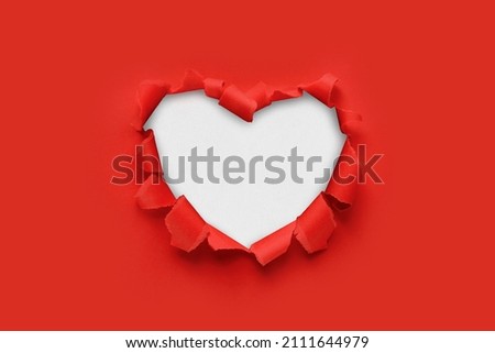 A paper hole with torn edges on a red background. Through paper. A ragged hole in the shape of a heart. Valentine's day. A symbol of love, romantic relationships. International Women's Day.