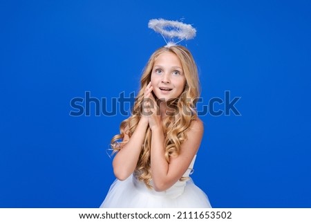 Angel girl with wings, valentine's day. Child with an angelic character. Little girl in an angel costume, white dress and feather wings on a blue background. The concept of an innocent child.