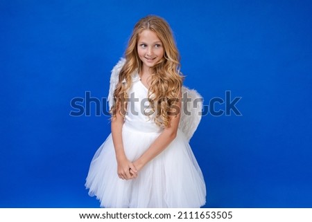 Postcard for valentine's day. Child in long white dress and with angel wings on a blue background. Happy angel girl over white. Beautiful young girl with angel wings