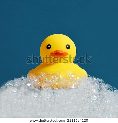 Yellow rubber duck toy floating on soap or shampoo bubble foam in the bath. Duckling in bubble bathtub with soapy foam. Royalty-Free Stock Photo #2111654120