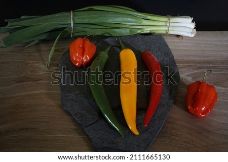 Hot peppers and habaneros in different colors on a wooden board in low light.