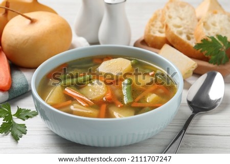 Bowl of tasty turnip soup and spoon on white wooden table, closeup