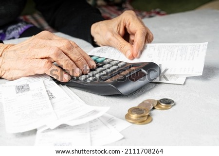 Lack of money in old age. Elderly woman wrinkled hands count receipts with calculator. Poverty in old age, small pension concept. Royalty-Free Stock Photo #2111708264