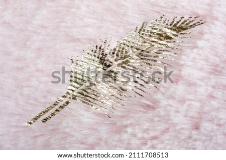 Print in the form of a golden feather on the surface of faux fur in pink.
