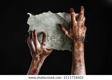 Hands of zombie with empty paper sheet on dark background