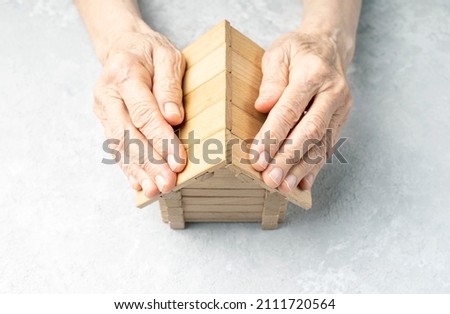 Wrinkled hands of an elderly woman protects the house. Taking care of your home concept. Royalty-Free Stock Photo #2111720564