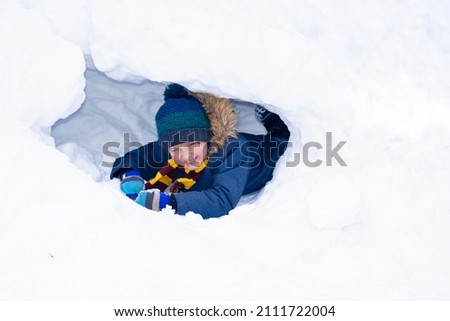 
happy laughing schoolboy lies in snow cave in winter outside
