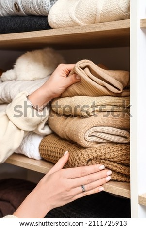 Woman taking warm sweater from shelf in wardrobe, closeup
