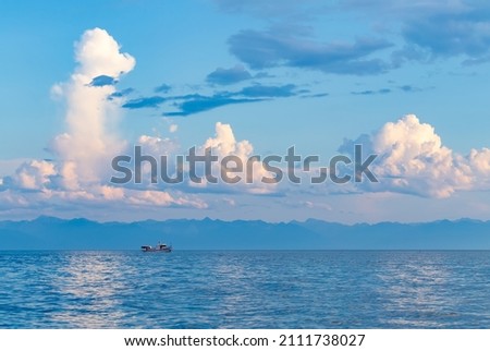 Landscape with white and pink cumulus clouds above lake at sunset. A white ship sailing on the water. Royalty-Free Stock Photo #2111738027