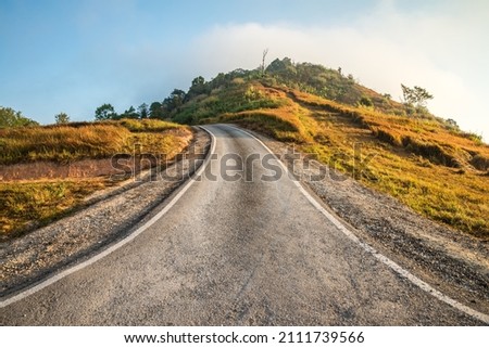 Beautiful asphalt country road side on the green mountain background in morning sunlight, Phetchabun Thailand. Road trip, travel holiday or transportation concept. Royalty-Free Stock Photo #2111739566