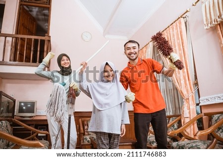 Excited father, mother and daughter holding cleaning tools