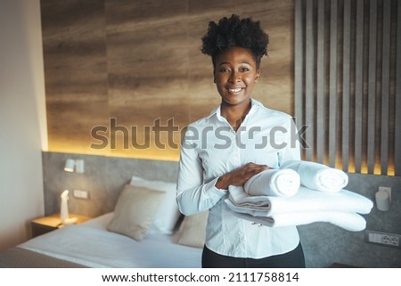 Maid working at a hotel holding towels and looking at the camera smiling - housekeeping concepts. Maid with fresh clean towels during housekeeping in a hotel room Royalty-Free Stock Photo #2111758814