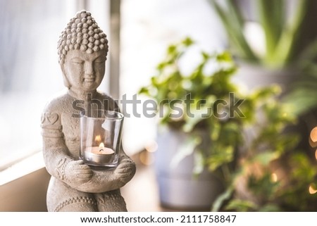 Spiritual awakening. Statue of Buddha and a small meditation. Zen spiritual ritual meditating white face of Buddha, brown candle on green floral background. Religion concept, esoterics.