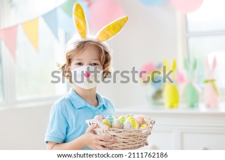 Easter egg hunt in covid 19 pandemic. Kid in bunny face mask. Coronavirus prevention during spring holiday. Child with eggs and rabbit ears. Safe Easter celebration for family with children.