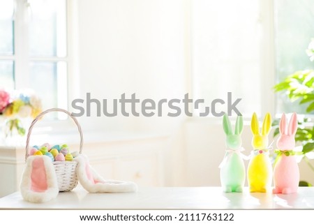Easter home decoration. Basket with colorful dyed eggs and rabbit ears, tulip flowers and wooden bunny for festive Easter celebration at home. Kids basket for Easter egg hunt.