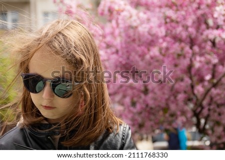 portrait of cute girl on sunny spring day, blossoming cherry tree in the background.