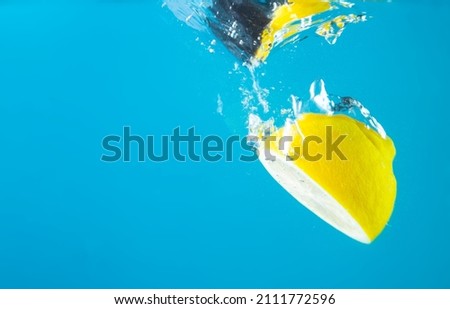  Cut fresh lemons in clear water with splash, blue background. High quality photo