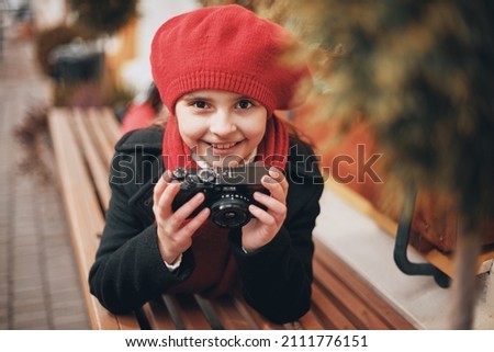a girl lies on her stomach on a bench on the street of the city with a camera in her hands. High quality photo