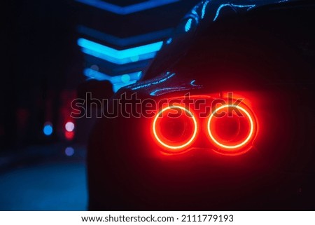 Supercar led taillight at the night city street, rear view close up red glow Royalty-Free Stock Photo #2111779193