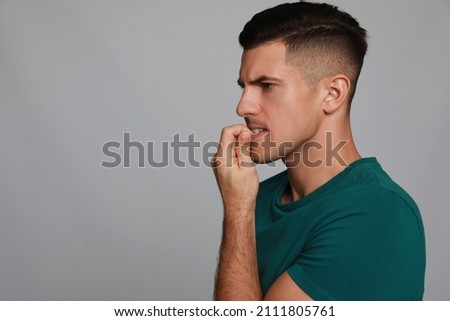 Man biting his nails on grey background, space for text. Bad habit Royalty-Free Stock Photo #2111805761