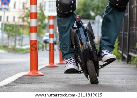 The beginning of riding an electric unicycle (EUC). A rider in protective gear tries to keep his balance on a monowheel. Royalty-Free Stock Photo #2111819015