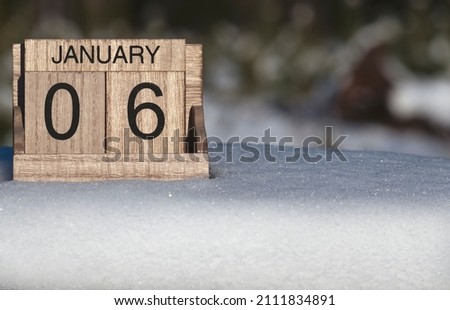 Wooden calendar of January 6 date standing in the snow in nature. 