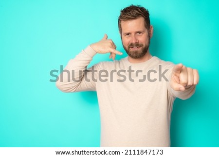 Young bearded man making call me gesture standing isolated over green background.