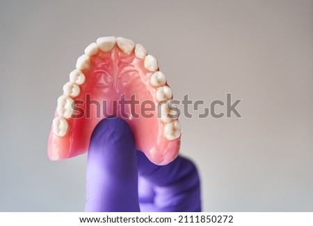 Fingers in purple gloves holding set of dentures. Dental plan concept. Royalty-Free Stock Photo #2111850272