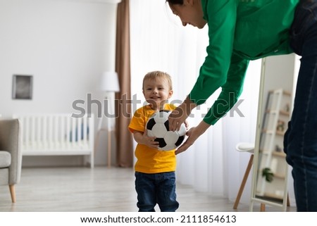 Happy caucasian mother and her toddler son playing with soccer ball at home, having fun and enjoying time together, free space. Maternity leave, childhood and leisure time concept Royalty-Free Stock Photo #2111854613