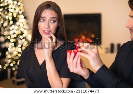 Unsuccessful Proposal Concept. Hopeful young man proposing to confused doubtful woman who is hesitating, scared lady looking frustrated thinking about refusal and breakup, not sure about marriage Royalty-Free Stock Photo #2111874473