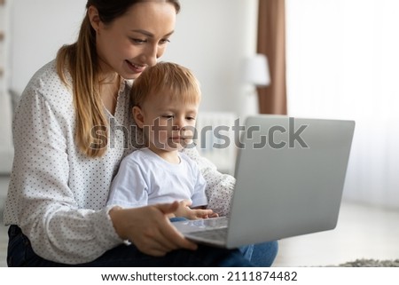 Happy single mother and little son using laptop online application, making video call or watching cartoons together, sitting in living room, copy space