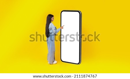 Full Body Length Back View Of Woman Using Big Smartphone With Blank White Screen Touching Display Panel With Finger, Cheerful Lady Standing On Yellow Background, Ordering Food Delivery, Mock Up Banner Royalty-Free Stock Photo #2111874767