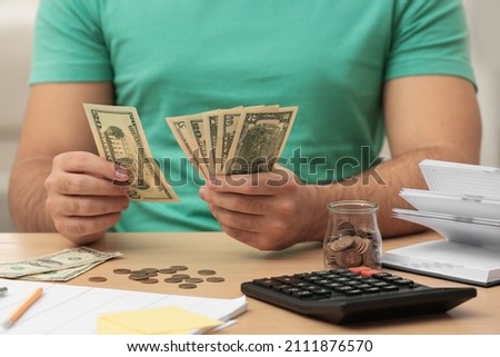 Young man counting money at wooden table indoors, closeup