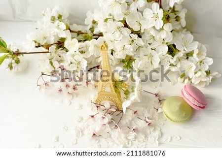 Eiffel tower figurine, macarons and branches with white cherry blossoms on a white background. Spring still life, travel France.