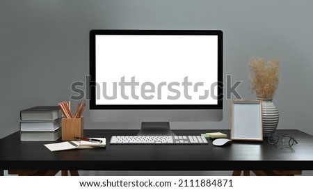 Modern workplace with computer pc, books, picture frame and supplies on black table.