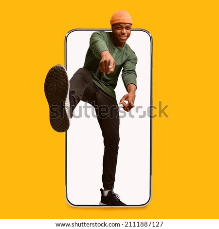 Cheerful young stylish attractive african american guy pointing fingers at camera on big phone empty screen isolated on yellow background, studio, collage. Your turn, great ad and offer, mobile app