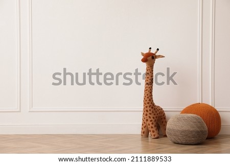 Toy giraffe and poufs near white wall indoors, space for text. Interior design
