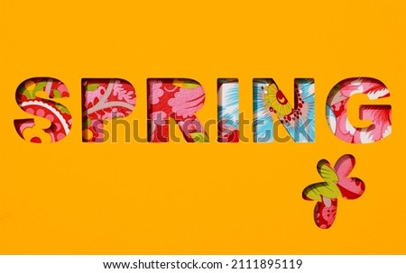 the text spring and a flower cut out on an orange paper, and a floral background seen through the cutout holes