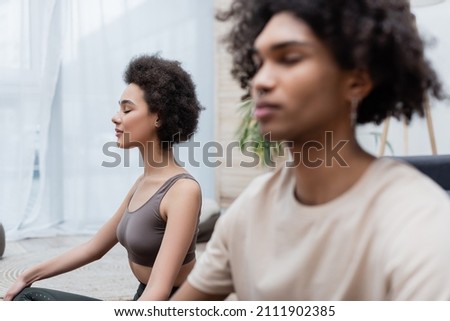 Young african american woman meditating near boyfriend in living room