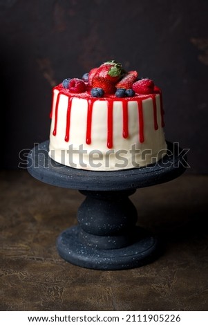 beautiful cake with fresh berries, raspberry, strawberry, blueberry, on a black cake pan, side view on dark brown table